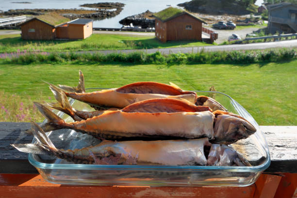 Smoked mackerel on glass dish against small Norwegian fishing village.