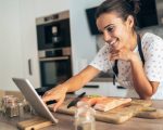 Young beautiful woman using digital tablet while cooking salmon filet in kitchen